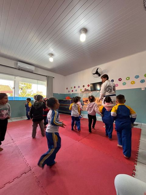 Crianças pequenas de uniforme escolar correndo sobre o tatame vermelho durante aula experimental em escola parceira