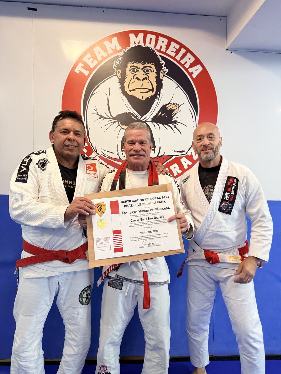 Faixas-coral e faixa-preta segurando certificado de graduação na academia Team Moreira