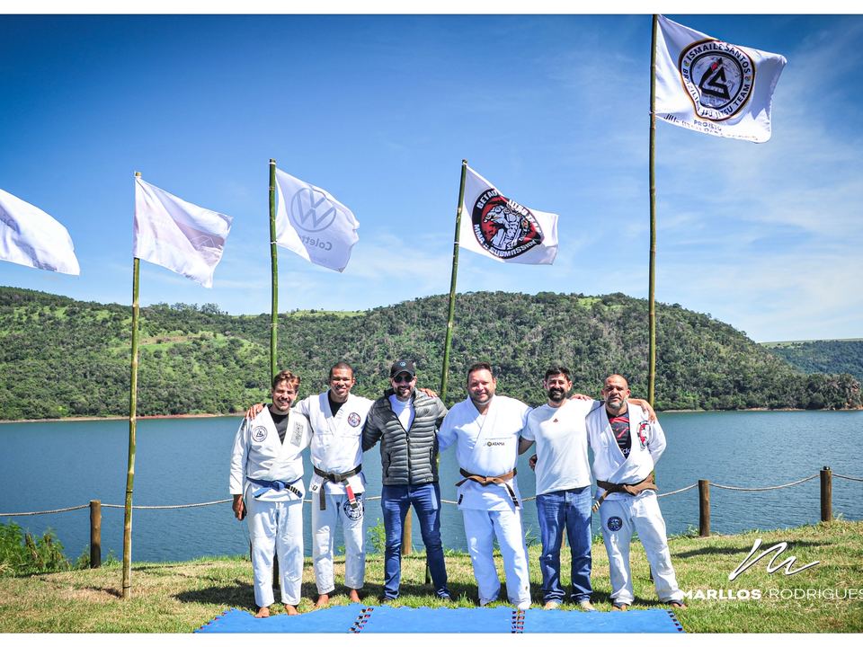 Professores faixa-preta do projeto reunidos entre bandeiras da equipe às margens da represa