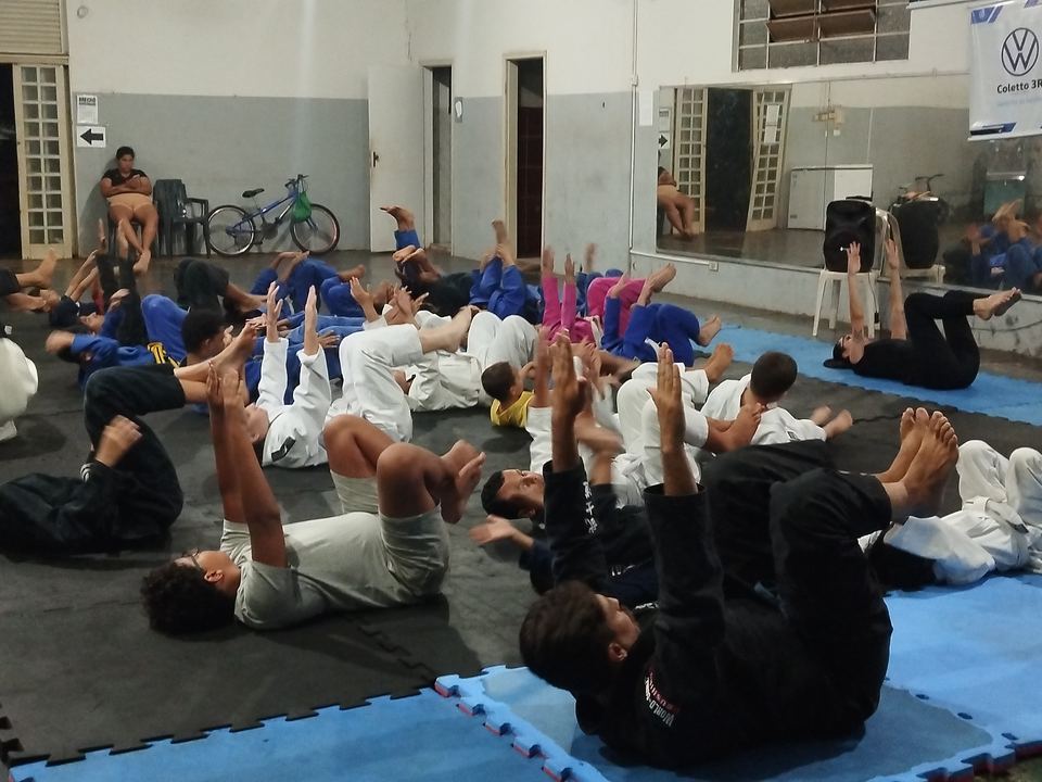 Alunos treinando em duplas no tatame durante aula em espaço coberto