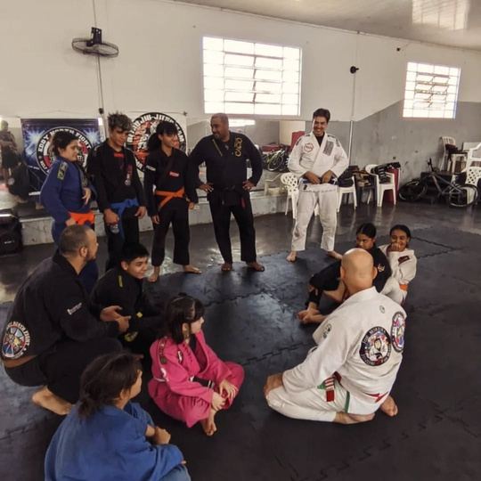 Crianças e professores sentados em roda no tatame durante a aula